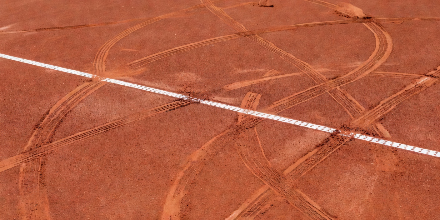 Red clay tennis court with a white baseline and visible sliding marks